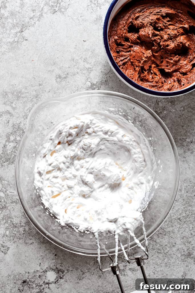 A bowl of freshly whipped cream positioned next to a bowl of the prepared chocolate filling, ready for folding.