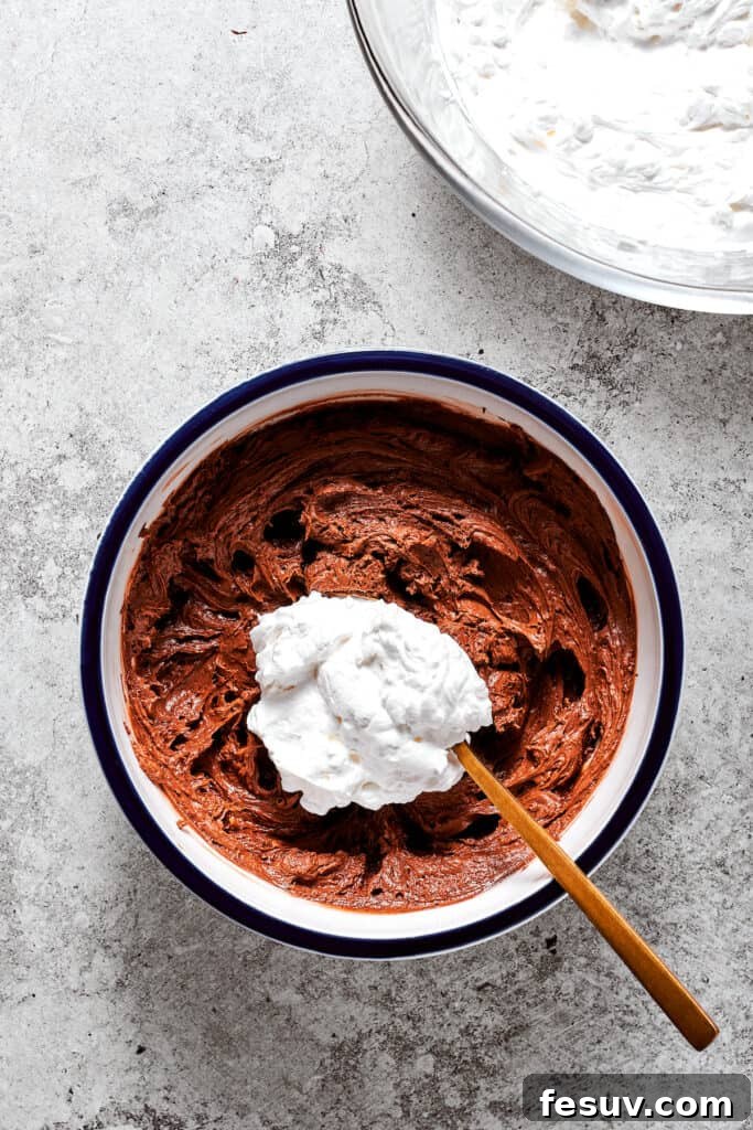 A spoonful of whipped cream being delicately folded into the rich chocolate filling in a bowl.