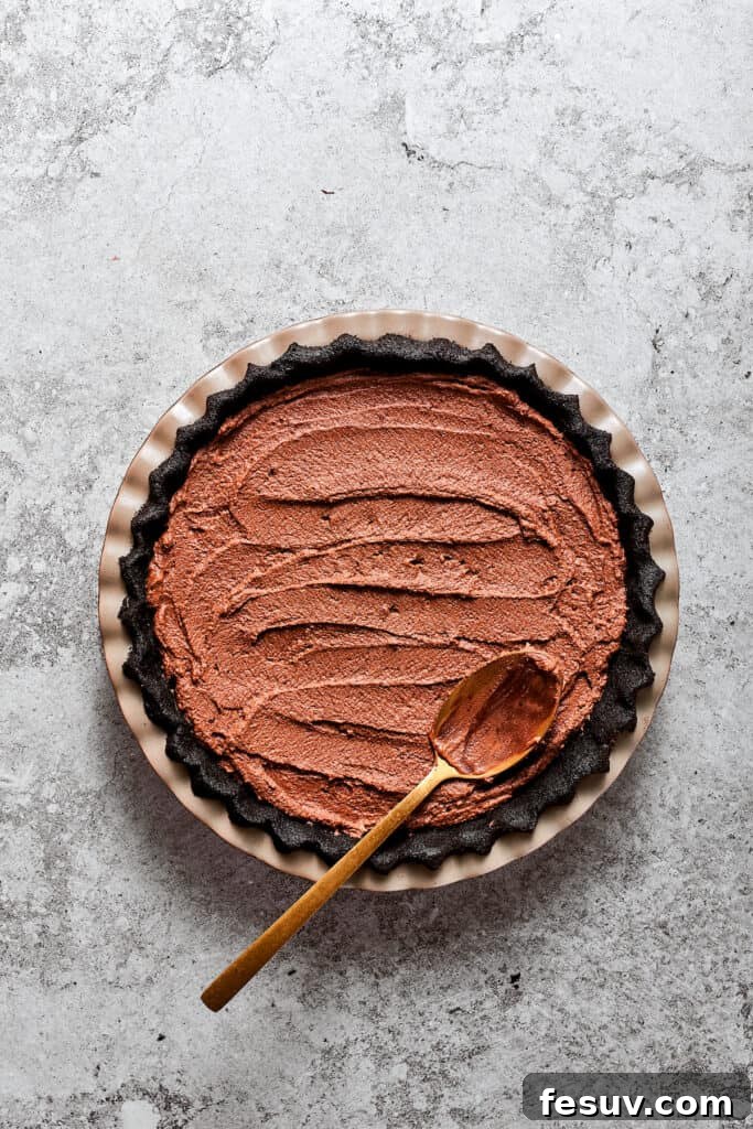 A spoon smoothing the luxurious French Silk Pie filling into the prepared Oreo crust in a pie dish.