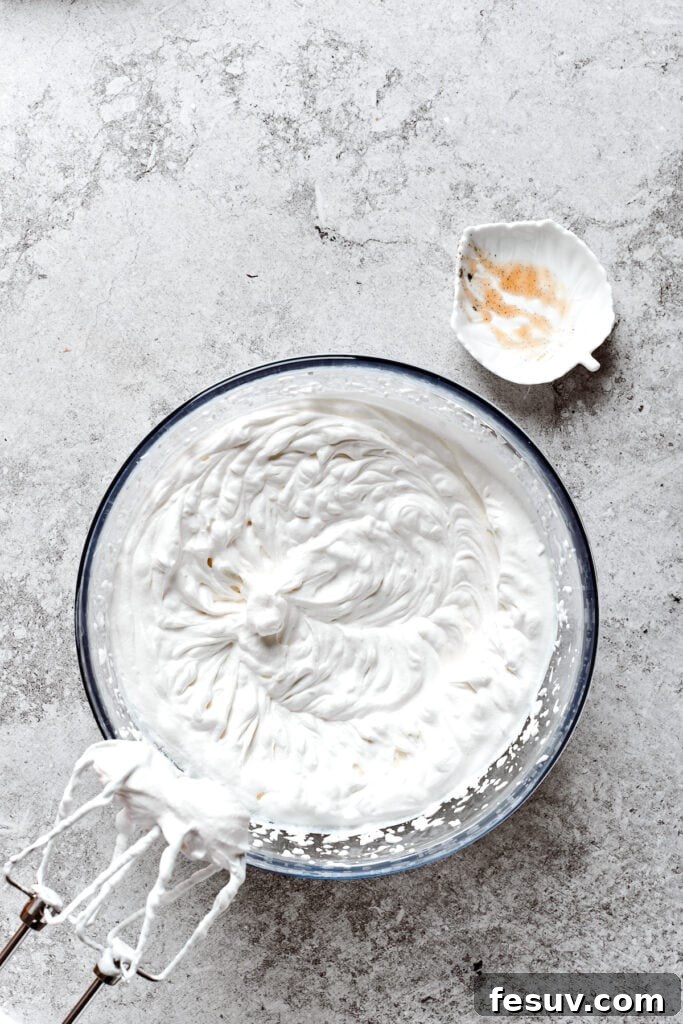 A bowl of freshly whipped cream with beater attachments resting above it, ready for the pie topping.