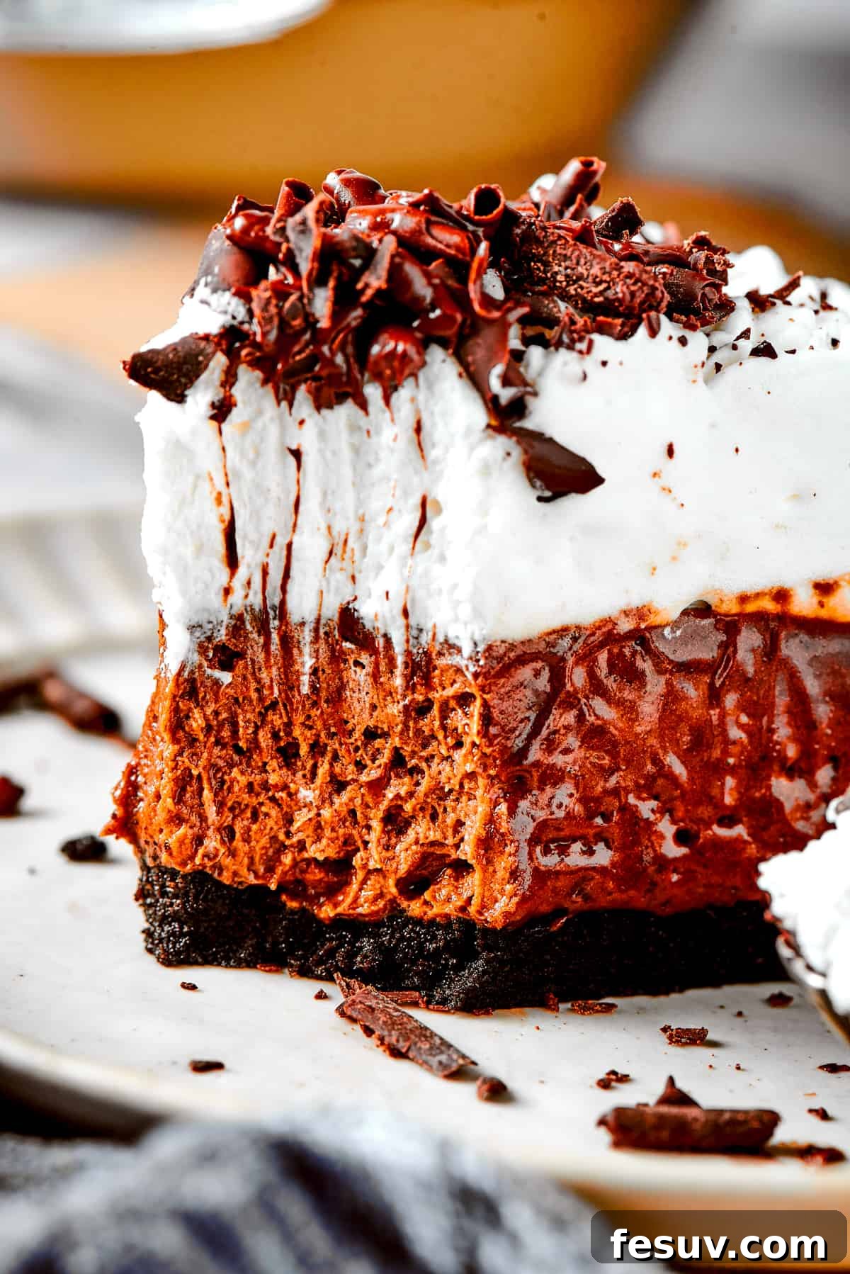 An inviting slice of French Silk Pie, rich with chocolate and topped with whipped cream, rests on a white plate with a fork taking a bite.