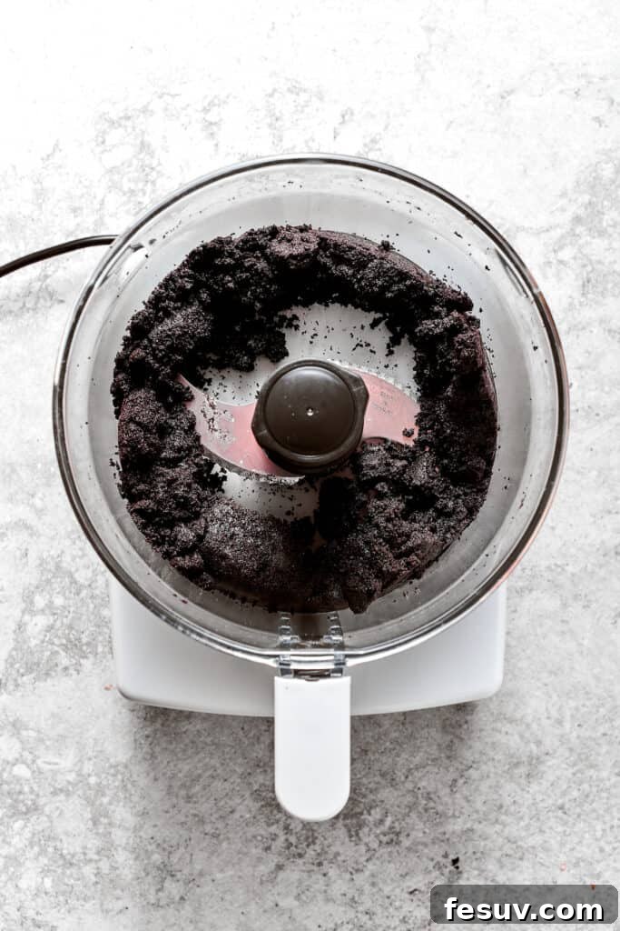 The food processor actively blending Oreo cookies and butter into fine, moist crumbs for the pie crust.