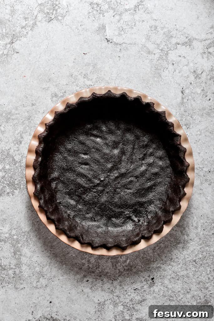 A freshly pressed Oreo cookie crust lining a nine-inch pie pan, ready for chilling.