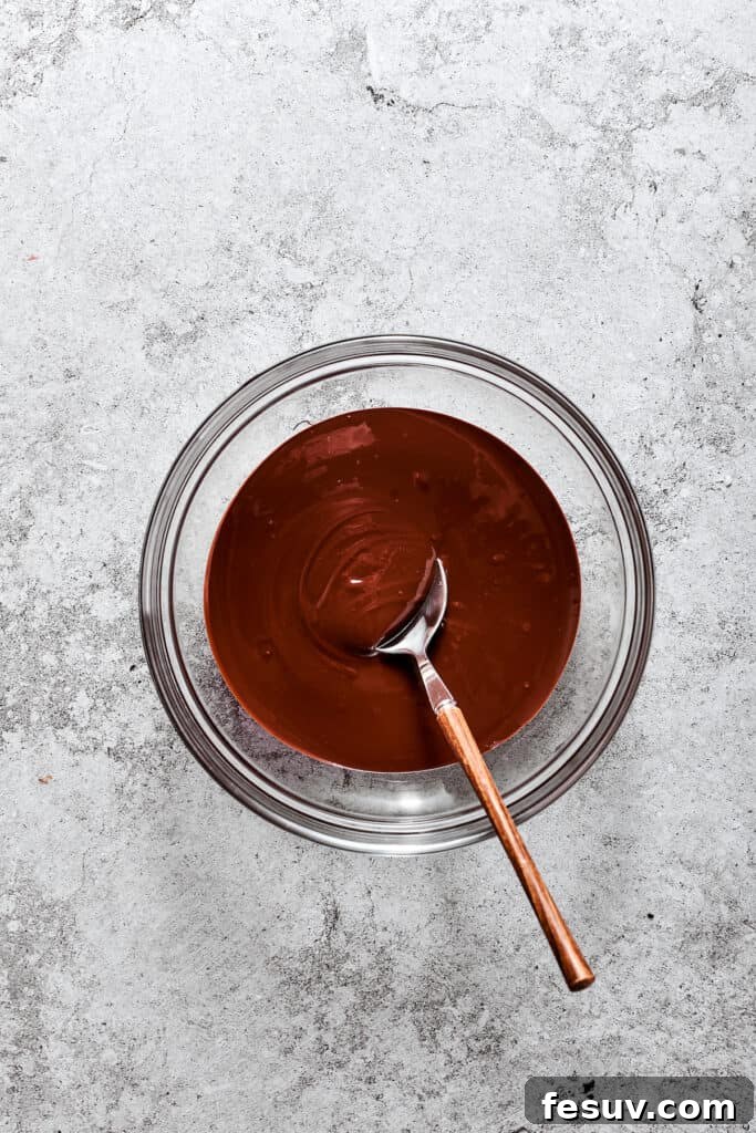 A bowl of melted bittersweet chocolate, glistening and smooth, with a wooden spoon resting inside.
