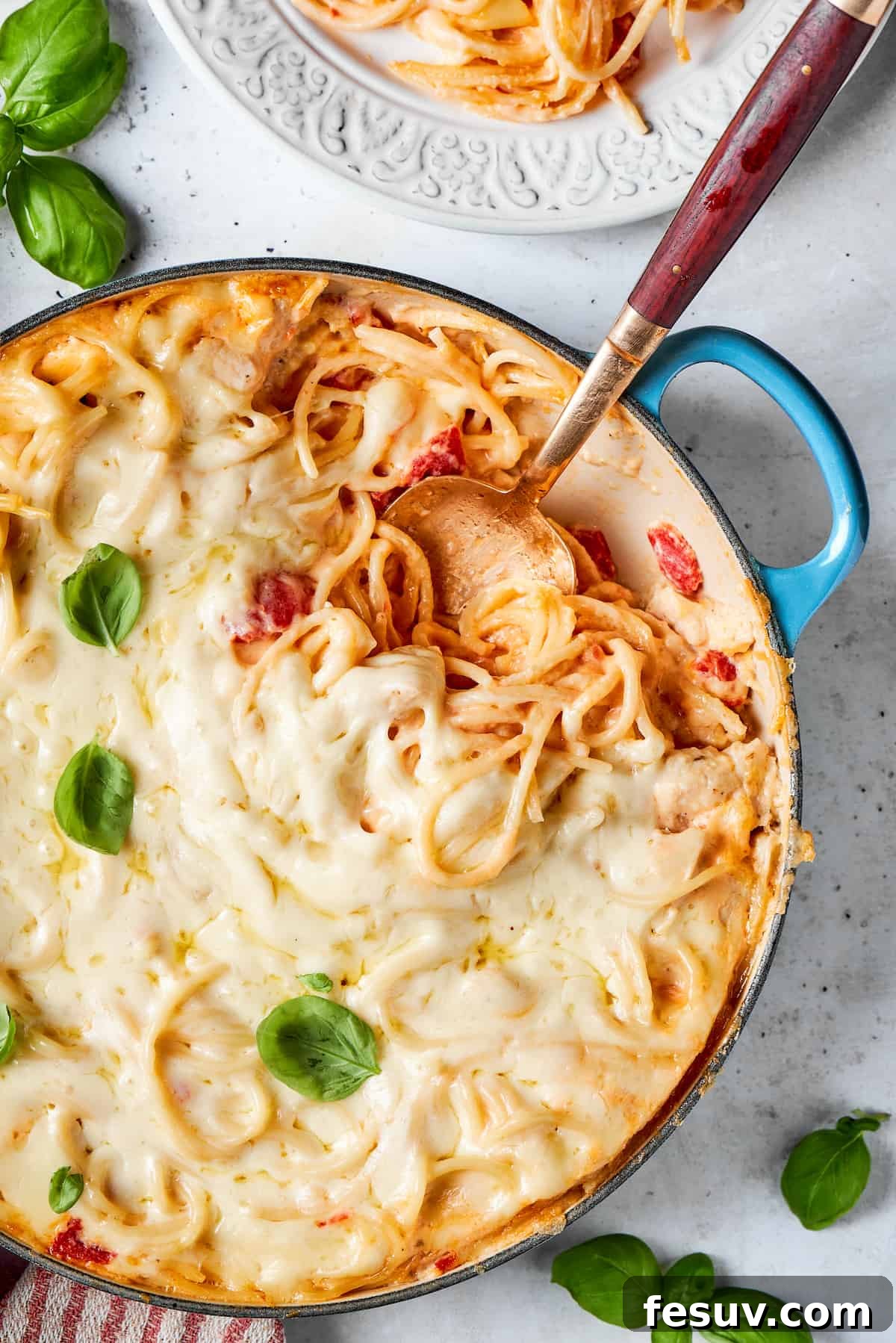 Fresh basil is used as a garnish on a pot of cheesy chicken spaghetti with a serving spoon inserted into the pot, ready to be served.