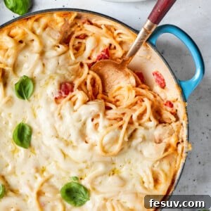 Fresh basil is used as a garnish on a pot of cheesy chicken spaghetti with a serving spoon inserted into the pot.