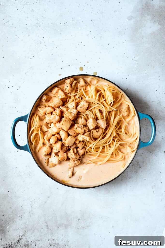 The cooked chicken and spaghetti are added to the rich, creamy sauce, ready to be combined.