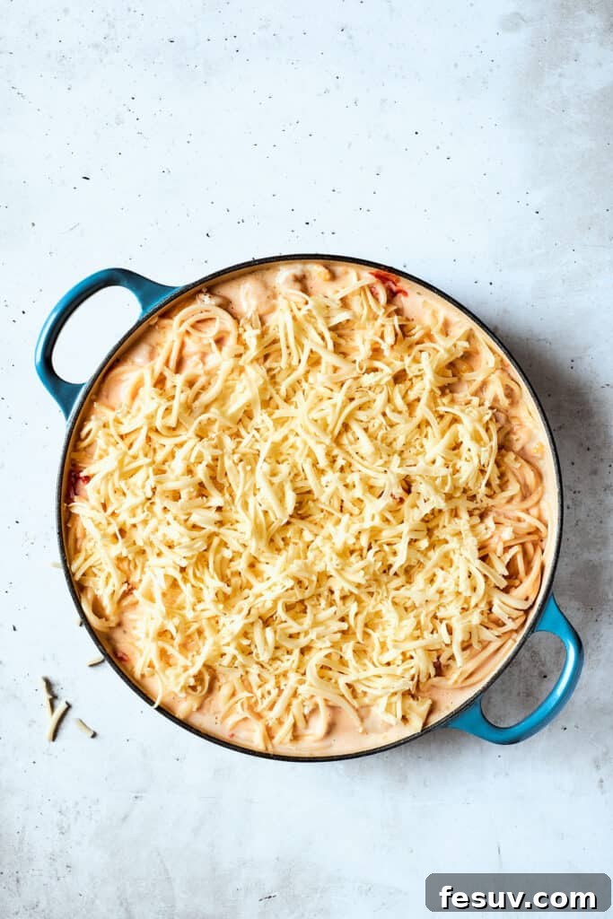 Mozzarella cheese is scattered generously over the top of the pot of pasta and chicken, ready for baking.