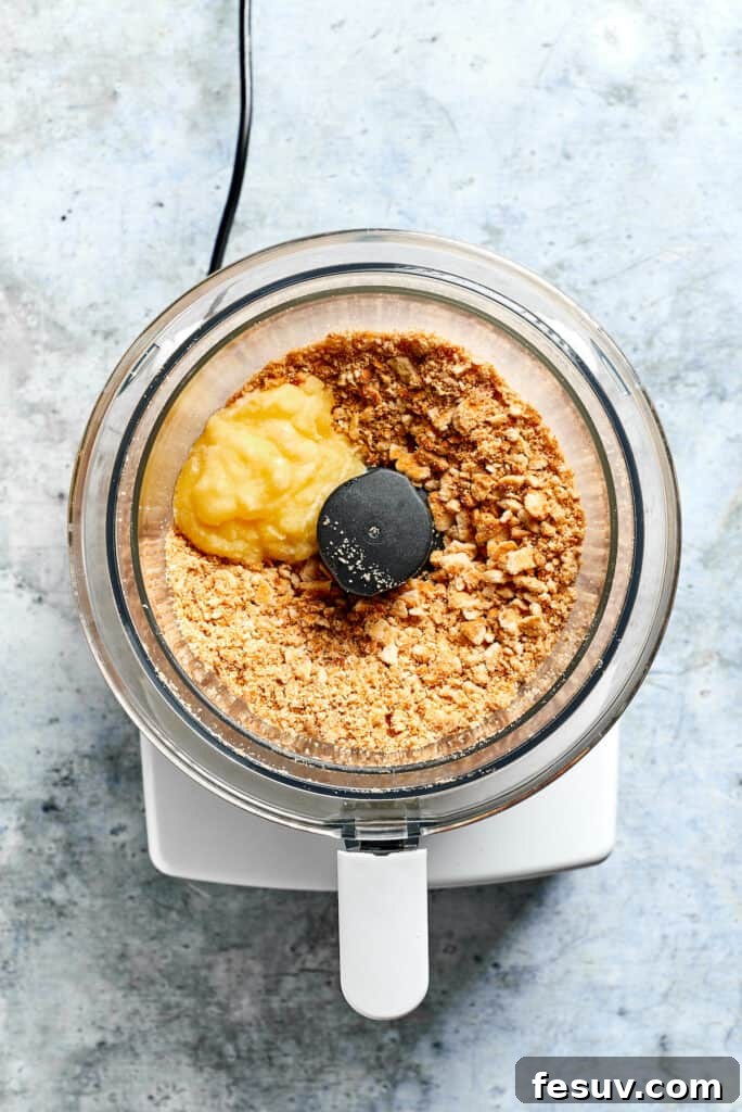 This creamy Poppy Seed Chicken casserole features a rich, poppyseed-flecked sauce that wraps cozily around tender shredded chicken. A food processor bowl containing Ritz crackers and melted butter, ready to be processed into a crunchy topping for the casserole.
