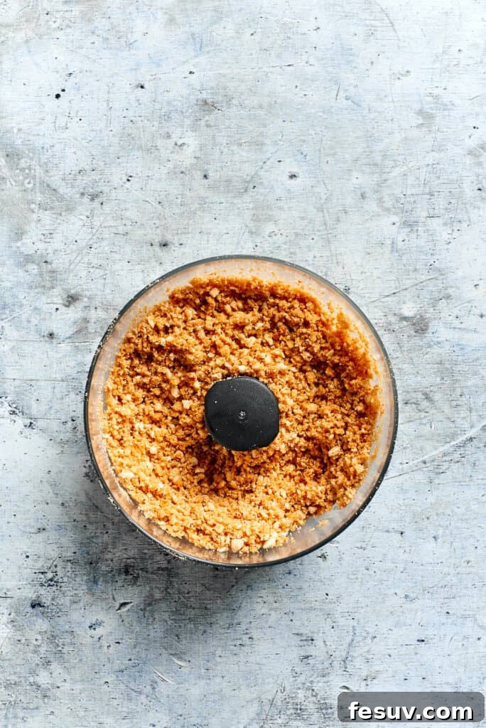 This creamy Poppy Seed Chicken casserole features a rich, poppyseed-flecked sauce that wraps cozily around tender shredded chicken. Close-up of golden, buttery Ritz cracker crumbs in a food processor, perfectly crushed and coated, ready to be sprinkled over the poppy seed chicken casserole.
