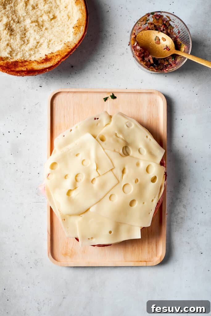 Slices of Swiss cheese being carefully placed to form a layer on the muffaletta sandwich.