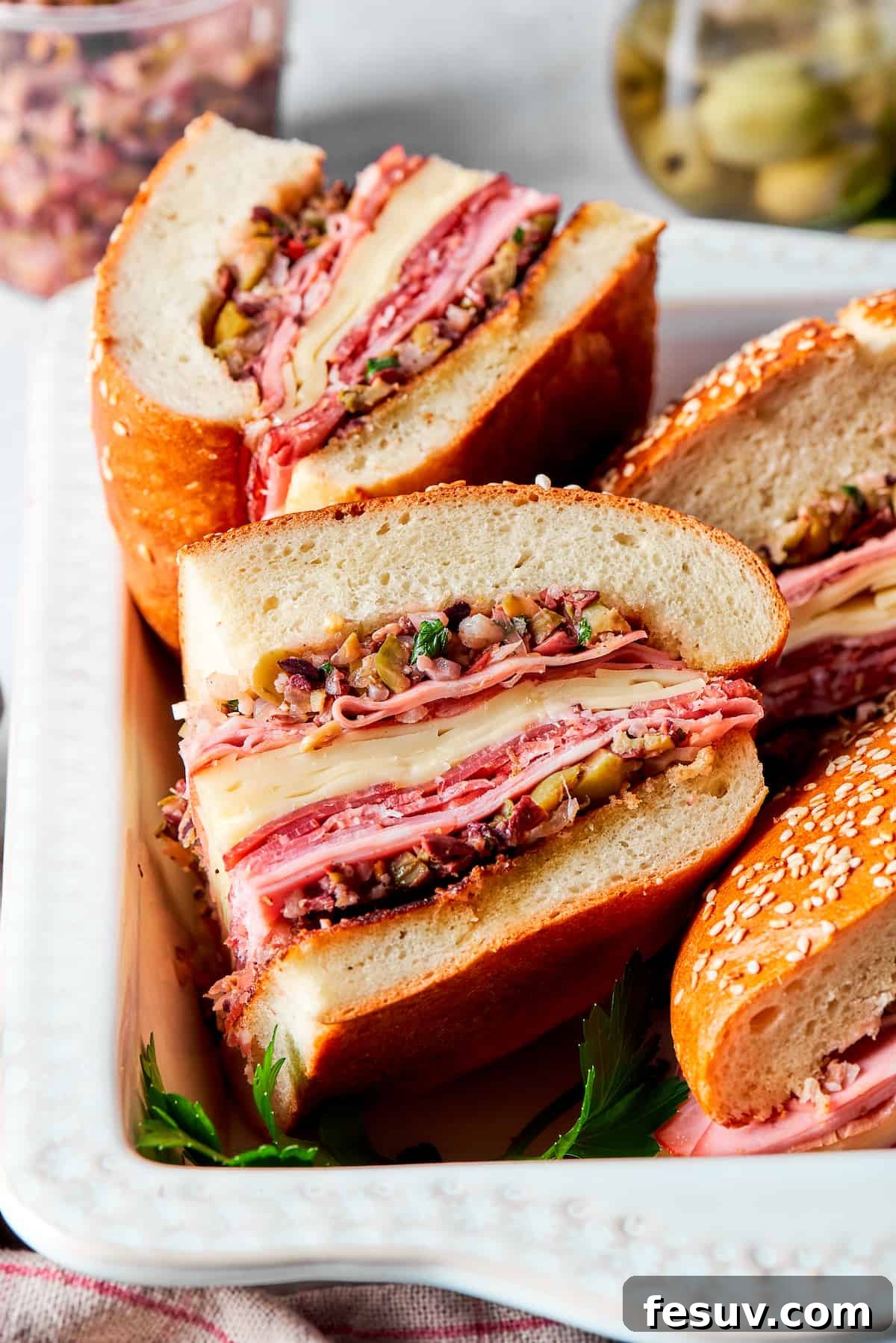 Several neatly cut pieces of muffaletta sandwich are arranged on their sides, clearly displaying the abundant layers of premium meats and cheeses within the soft bread.