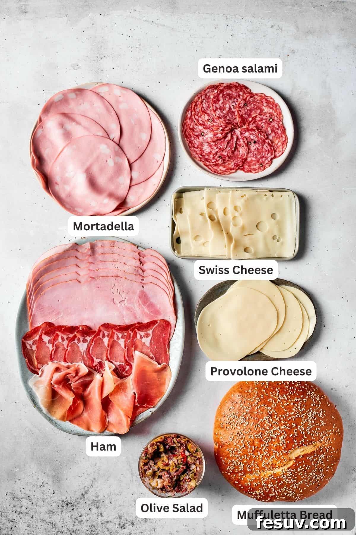 A selection of muffaletta sandwich ingredients: slices of mortadella, salami, ham, prosciutto, Swiss cheese, and Provolone cheese, neatly arranged.