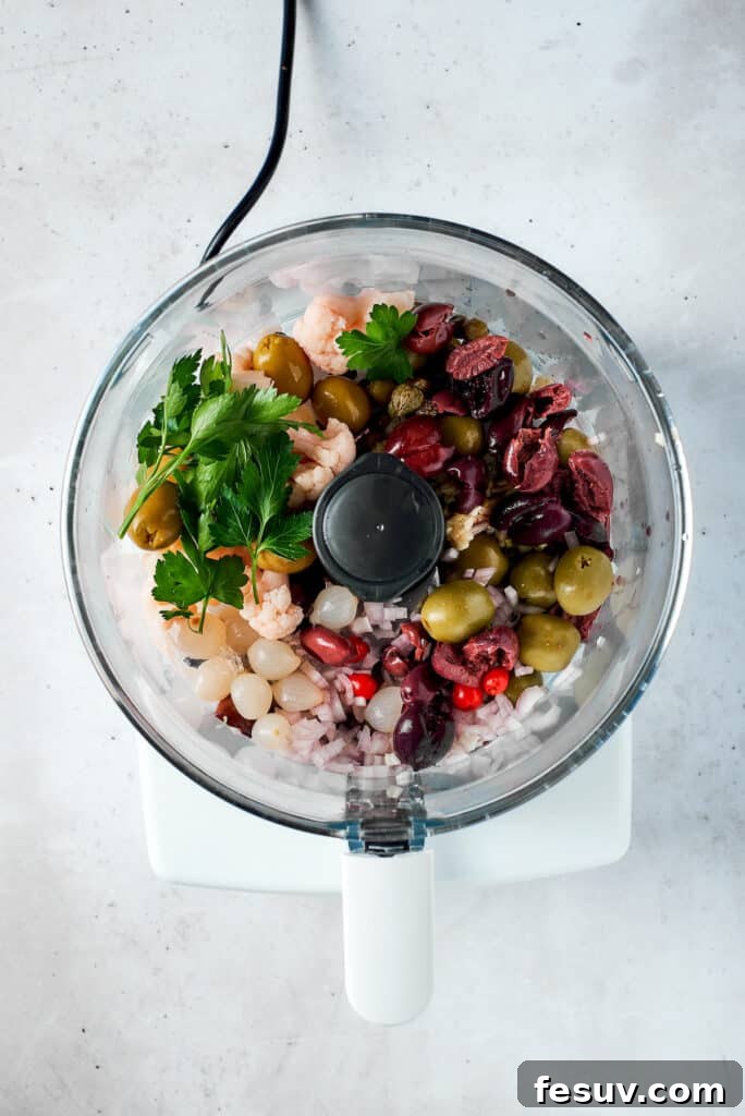 Various olive salad ingredients being added to a food processor bowl.