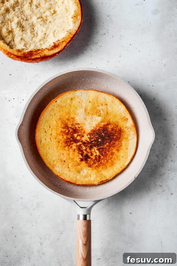 One half of a muffaletta bread loaf being lightly toasted in a skillet.