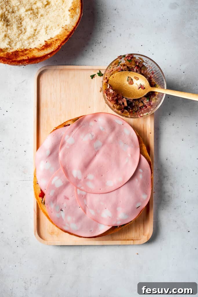 The final slices of mortadella being carefully placed on top of other deli meats in the sandwich layers.