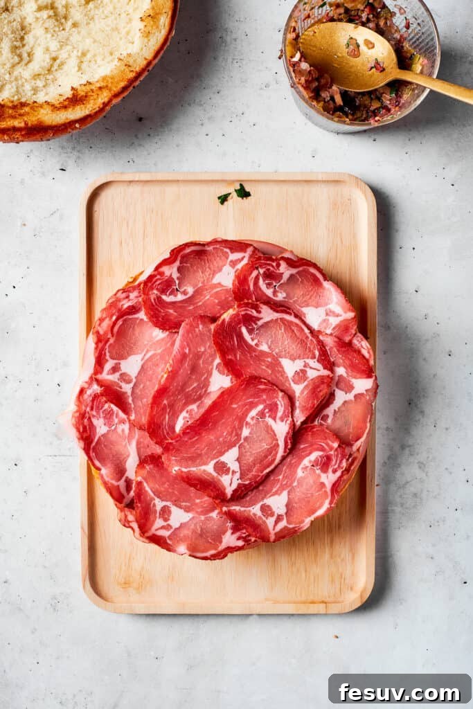 A layer of thinly sliced deli ham added to the stacked ingredients of the muffaletta sandwich.