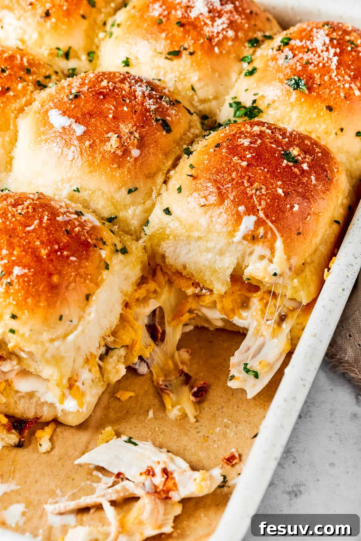 Golden brown Chicken Bacon Ranch Sliders, fresh from the oven, showcasing a perfect melty cheese topping. Toasted chicken bacon ranch sliders in a baking pan, golden brown with melted cheese and fresh parsley garnish.