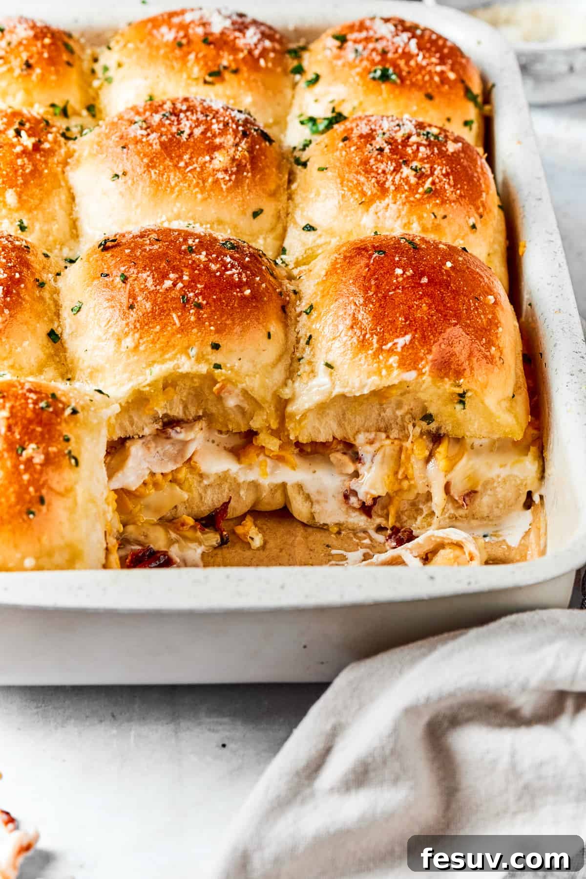 A closer view of the delicious, melty interior of the Chicken Bacon Ranch Sliders. Chicken sliders in a baking dish with two of the sliders exposed to show the rich, melty chicken, bacon, and ranch mixture inside, ready to be served.
