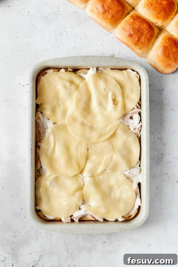 Placing smooth Provolone slices over the filling. Smooth, delicate slices of Provolone cheese are carefully laid over the chicken and ranch mixture, establishing a foundational layer that will melt beautifully into a creamy, savory component.