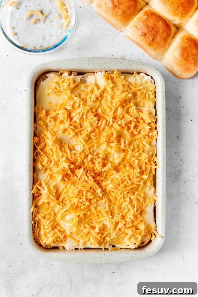 Spreading a liberal amount of shredded cheddar cheese. A generous, even blanket of shredded cheddar cheese is sprinkled over the Provolone, adding rich color and robust, familiar flavor to the developing slider masterpiece.