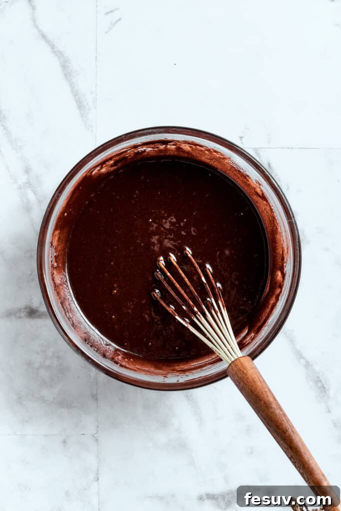 Mixing the brownie ingredients until perfectly smooth. A whisk smoothly blending the brownie batter in a mixing bowl.