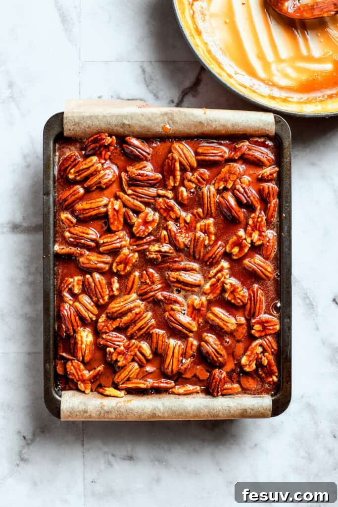 Pouring the pecan pie mixture over warm brownies for the final bake. The luscious pecan pie filling being generously spread over the warm, baked brownies.