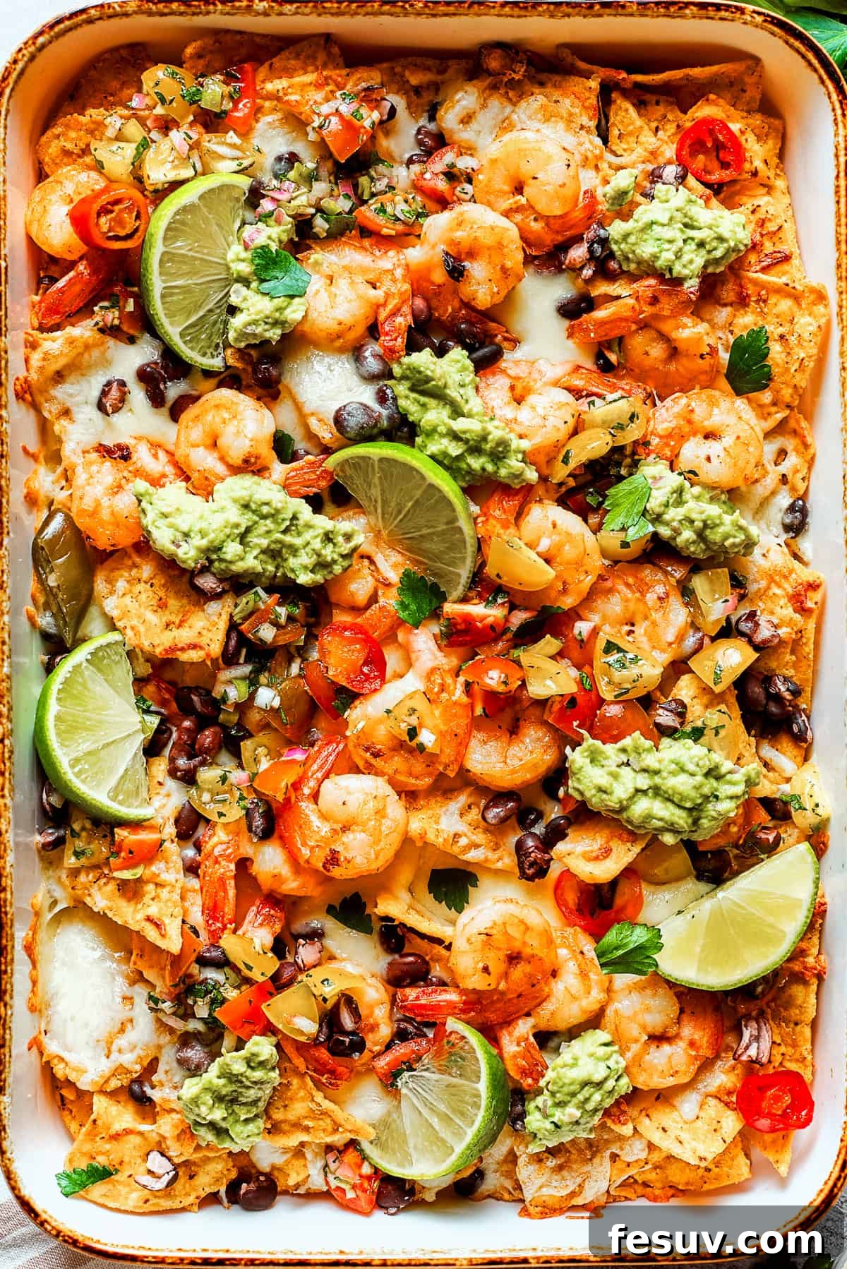 These crispy-crunchy Shrimp Nachos are piled with layers of flavor from creamy guacamole, juicy shrimp, and spicy, fresh pico de Gallo. Nacho chips topped with shrimp, cheese, black beans, tomatoes, and a garnish of guacamole and slices of lime.
