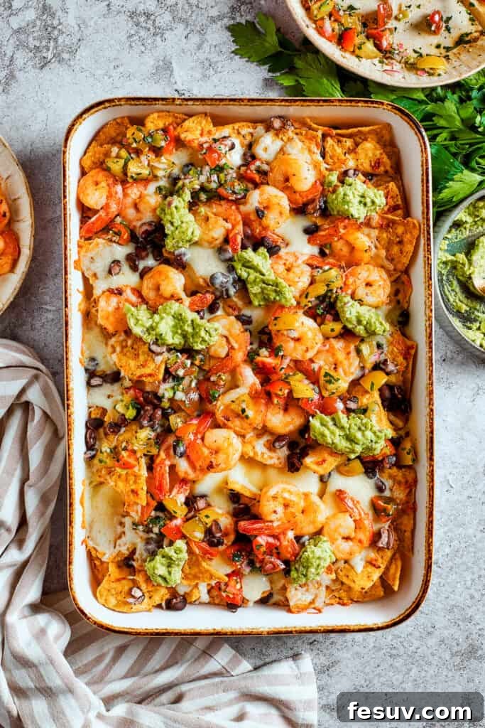 These crispy-crunchy Shrimp Nachos are piled with layers of flavor from creamy guacamole, juicy shrimp, and spicy, fresh pico de Gallo. Guacamole is dolloped onto the tray of shrimp nachos.