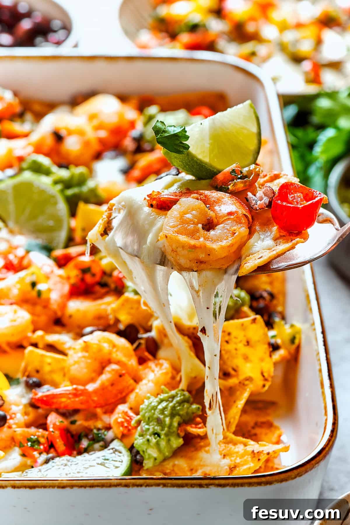 These crispy-crunchy Shrimp Nachos are piled with layers of flavor from creamy guacamole, juicy shrimp, and spicy, fresh pico de Gallo. A spoon lifts out a cheesy portion of shrimp nachos.