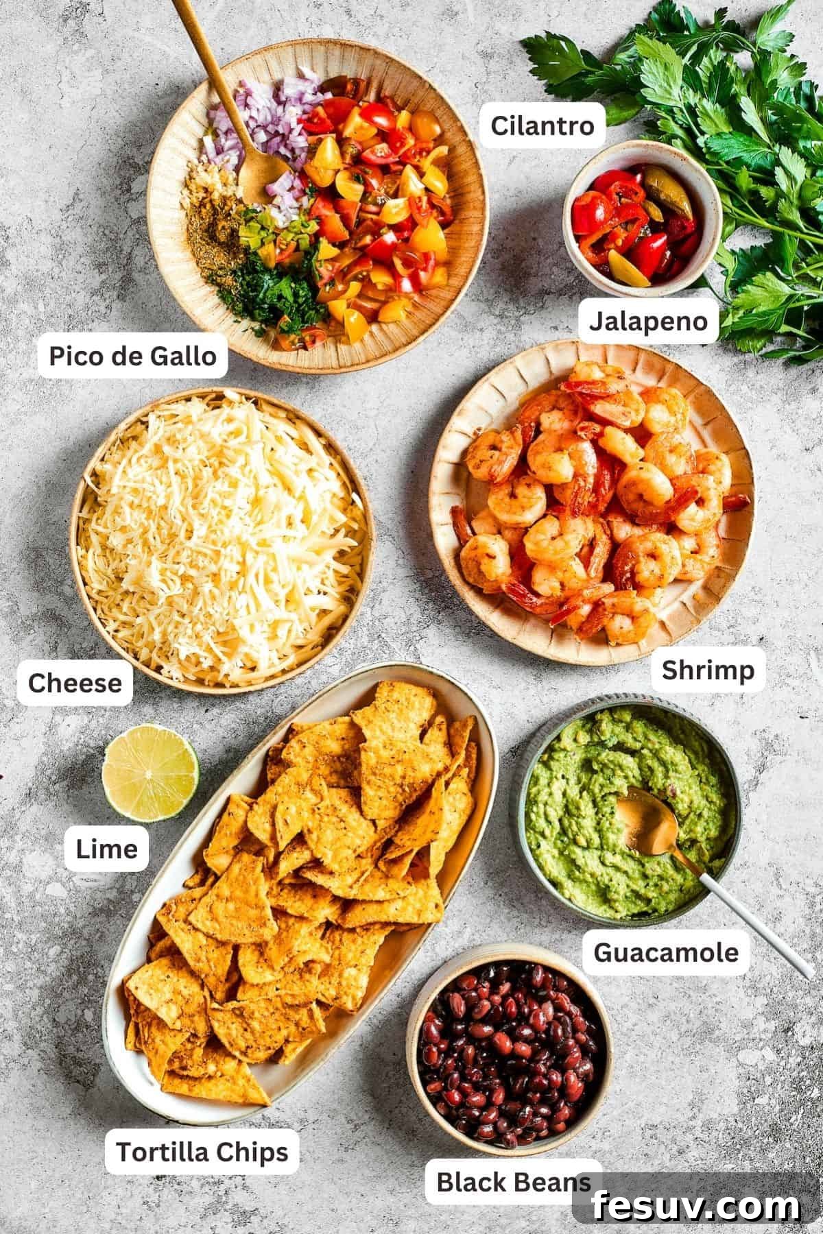 These crispy-crunchy Shrimp Nachos are piled with layers of flavor from creamy guacamole, juicy shrimp, and spicy, fresh pico de Gallo. Ingredients for shrimp nachos are shown: tortilla chips, pico de Gallo, guacamole, shrimp, lime, cheese, jalapeno.
