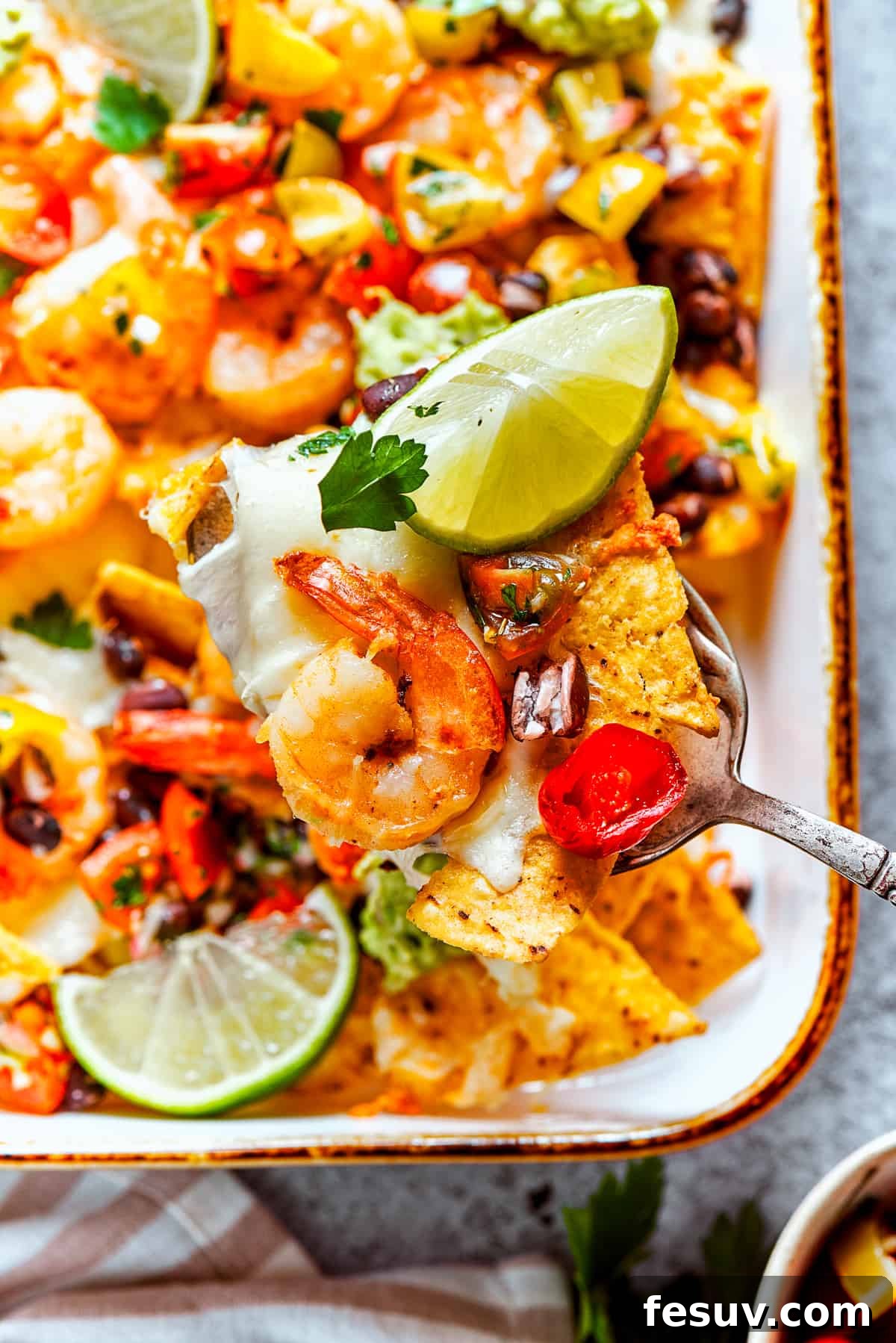 These crispy-crunchy Shrimp Nachos are piled with layers of flavor from creamy guacamole, juicy shrimp, and spicy, fresh pico de Gallo. A spoon lifts out nachos from a baking dish.
