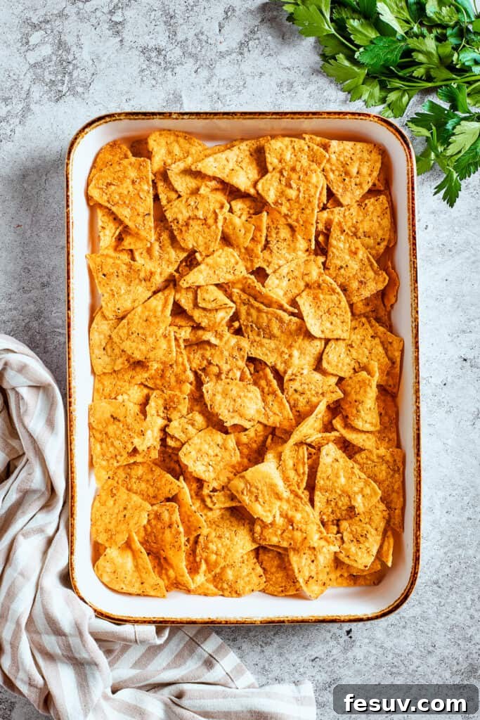 These crispy-crunchy Shrimp Nachos are piled with layers of flavor from creamy guacamole, juicy shrimp, and spicy, fresh pico de Gallo. Nachos are arranged in a baking tray.