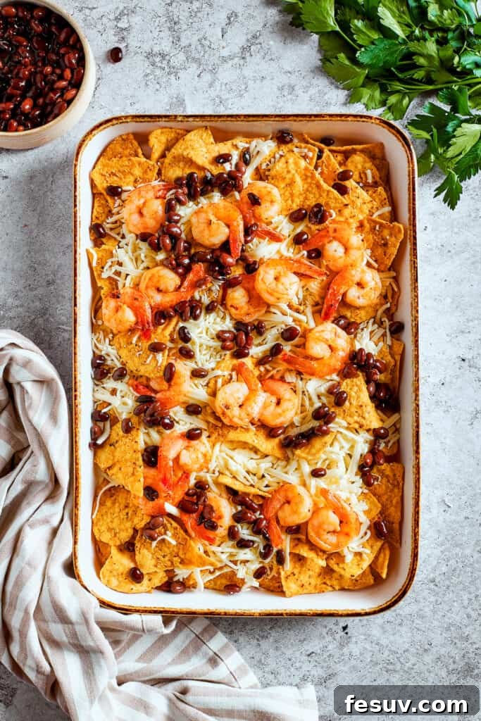 These crispy-crunchy Shrimp Nachos are piled with layers of flavor from creamy guacamole, juicy shrimp, and spicy, fresh pico de Gallo. Toppings are scattered over the top of the nachos.