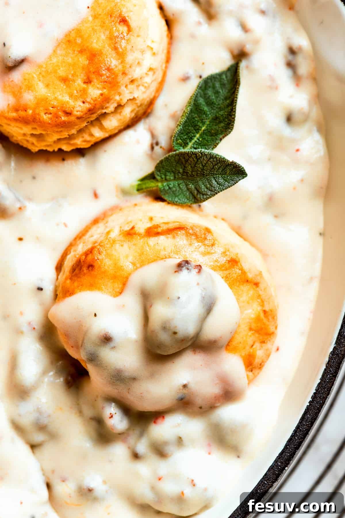 Close-up image of biscuits topped with sausage gravy. A close-up view of two golden-brown biscuits generously smothered in a thick, creamy, and chunky sausage gravy, showcasing the irresistible texture and savory appeal of the dish.