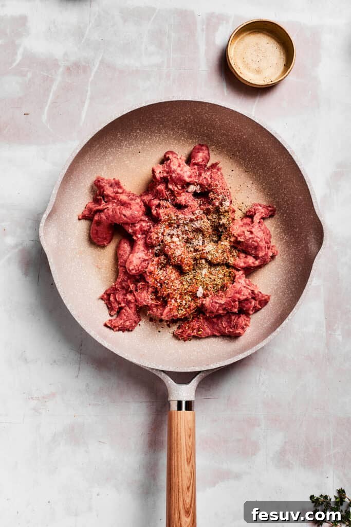 Adding sausage and herbs to a pan. Crumbled breakfast sausage being added to a hot skillet, ready to be browned and seasoned for the gravy base.