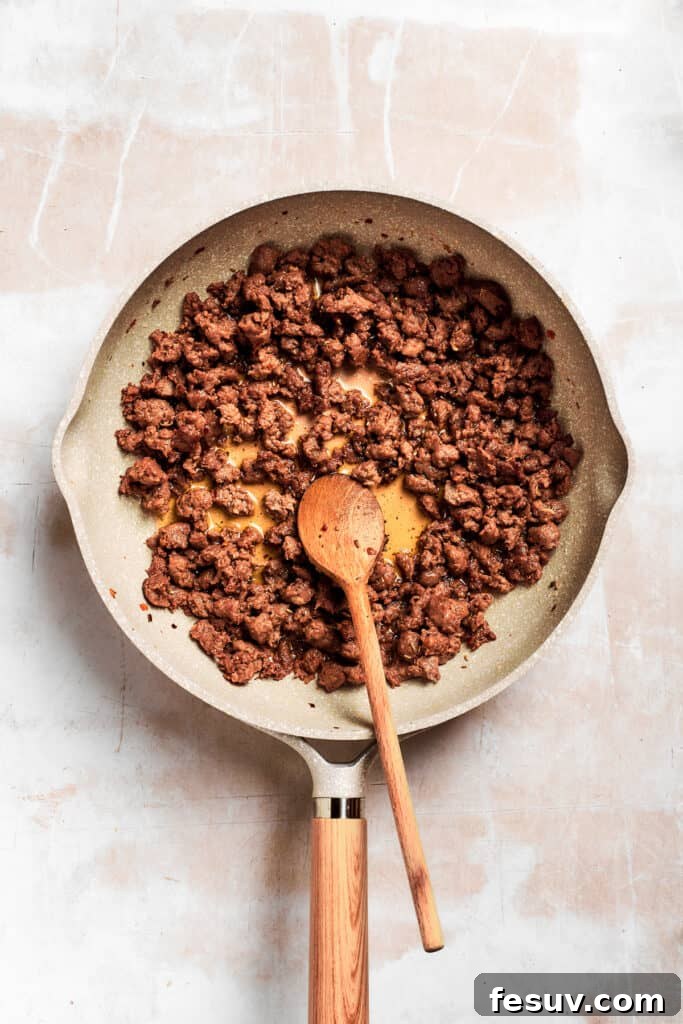 A wooden spoon stirs the pan of sausage. A wooden spoon stirs the crumbled, seasoned breakfast sausage as it browns evenly in the skillet, releasing its rich flavors to form the foundation of the gravy.