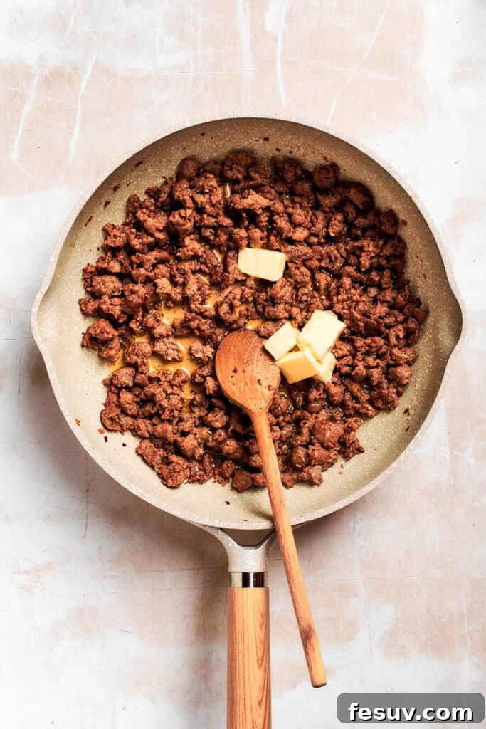 Butter is added to the sausage in the pan. Melted butter being added to the browned breakfast sausage in a skillet, creating the foundational fat for the roux in the creamy gravy.