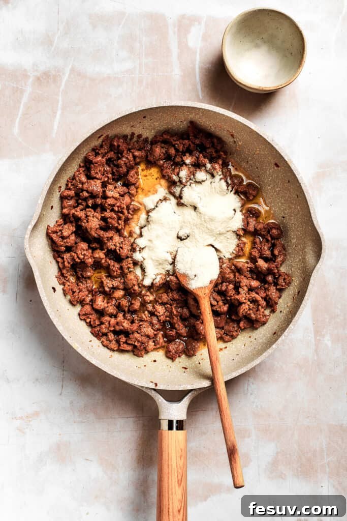 Flour is added into the pan. All-purpose flour being sprinkled over the melted butter and browned sausage in a skillet, forming the base of a flavorful roux for the sausage gravy.
