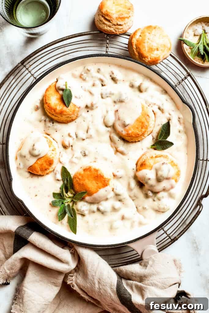 Five biscuits rest in a pan of sausage and gravy. A close-up shot of a skillet filled with rich, creamy sausage gravy, with several golden-brown homemade biscuits nestled directly into the gravy, ready to be served.