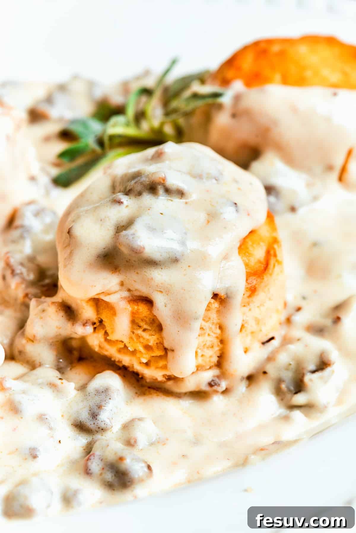 Sausage gravy poured over biscuits. A golden-brown biscuit sliced in half, generously topped with a rich, creamy, and chunky sausage gravy, highlighting the delightful texture and warmth of this classic comfort dish.