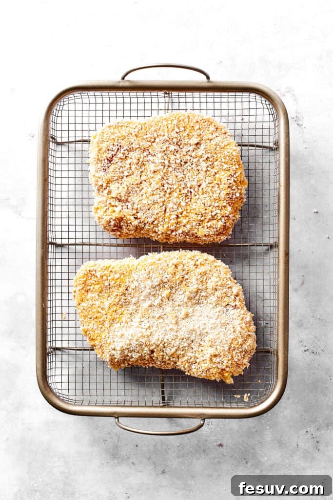 Breaded pork cutlets resting on a wire rack before frying.