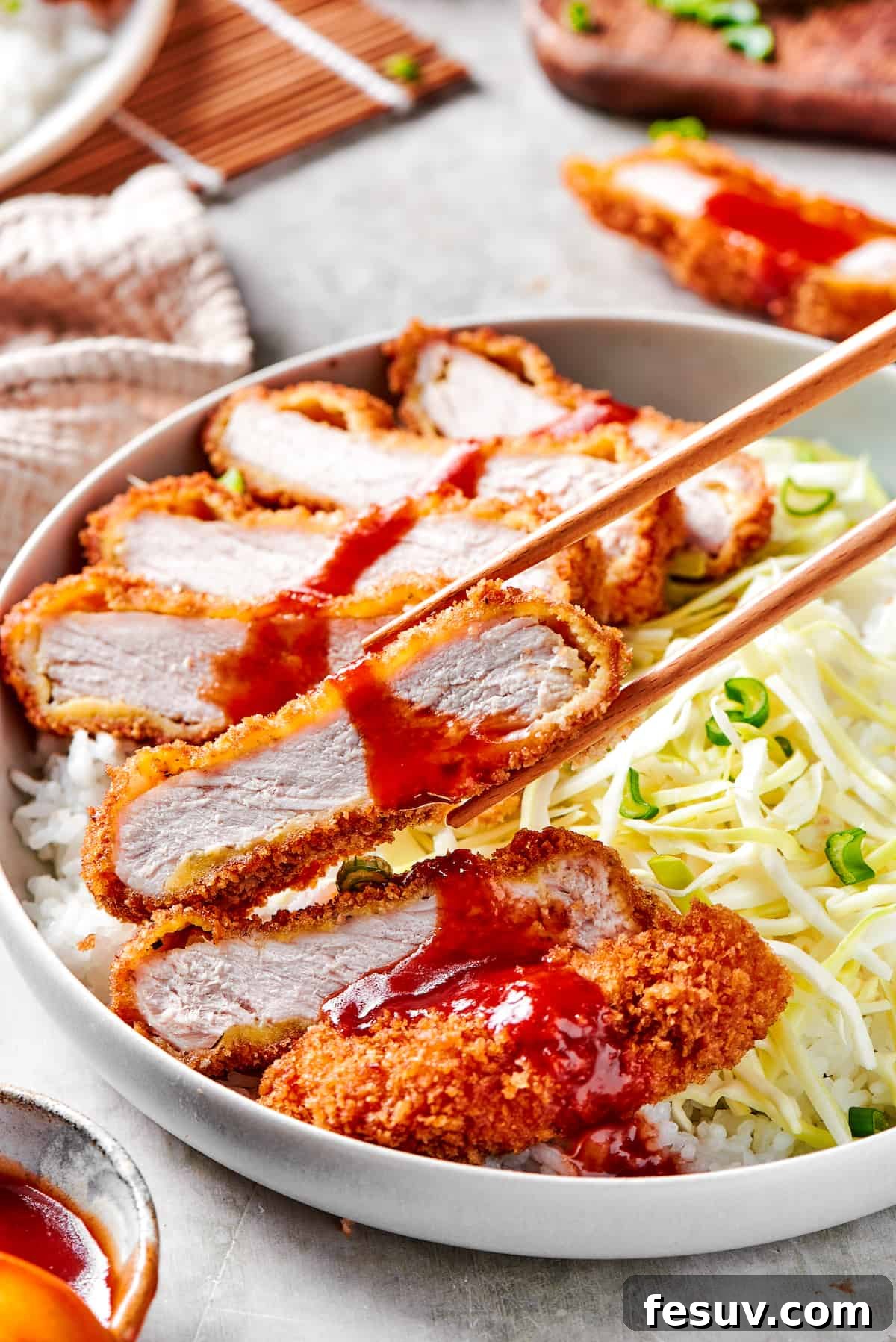 Chopsticks lifting a piece of perfectly fried and sliced Pork Katsu.