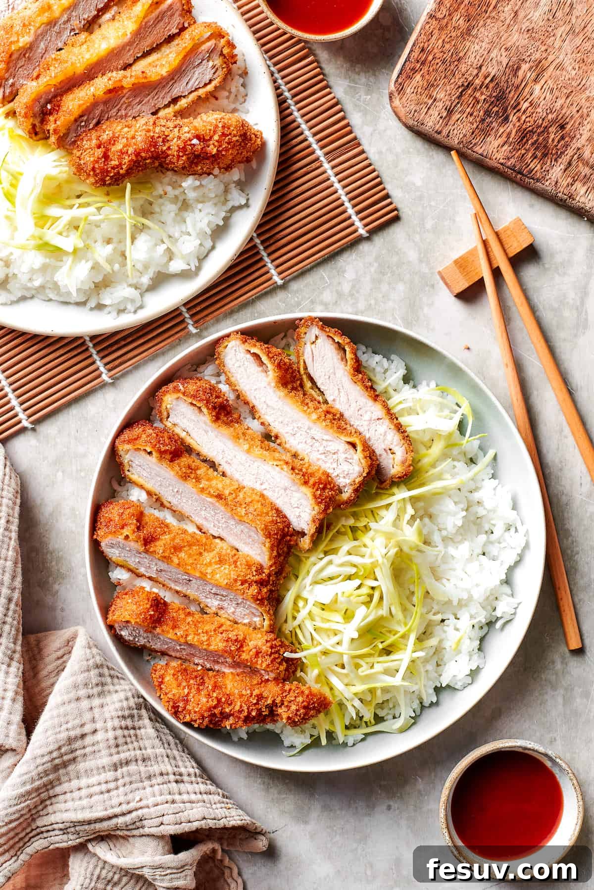 Japanese Pork Katsu, sliced and served with shredded cabbage and white rice on dinner plates.