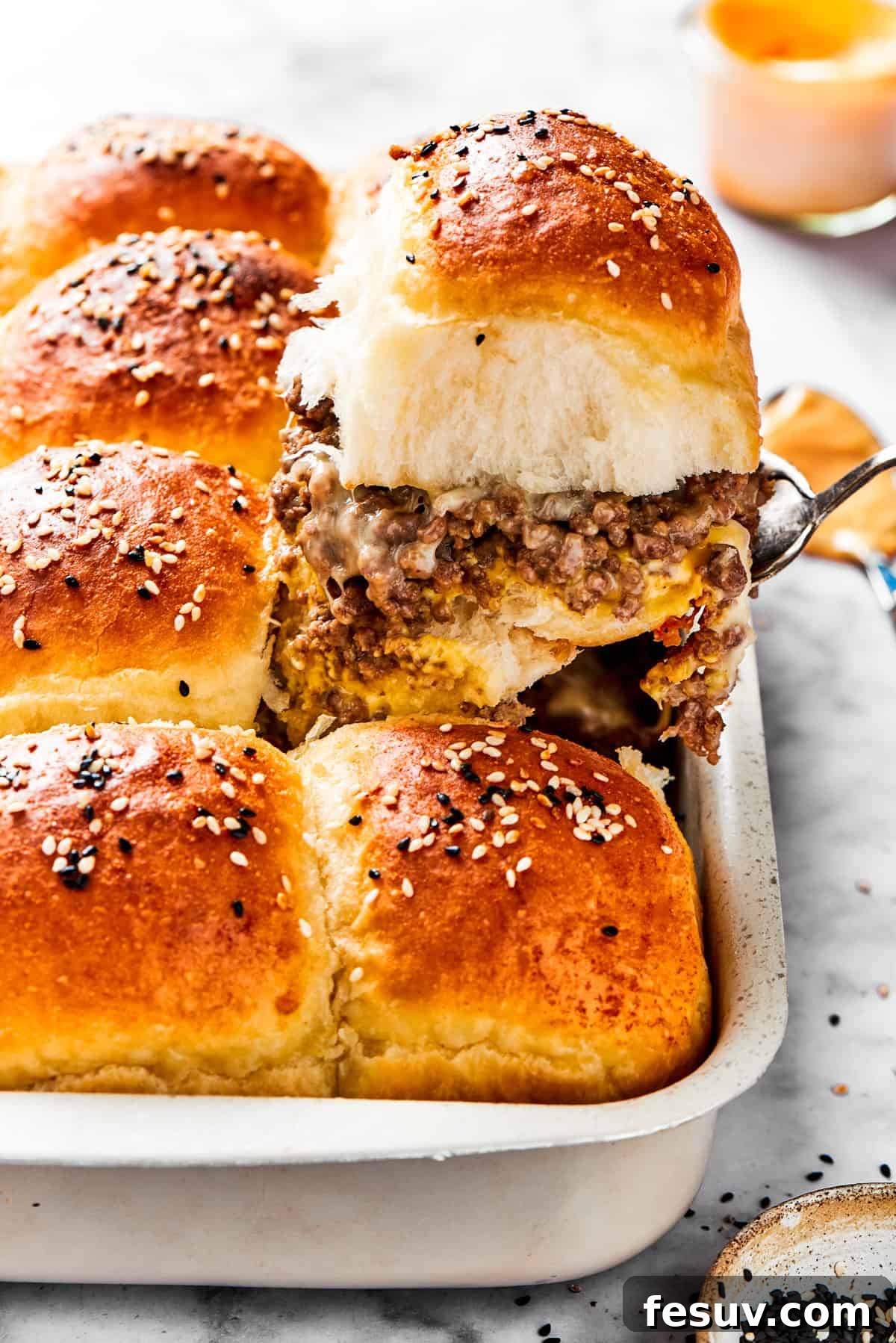 A spatula holding up a slider filled with ground meat and melted cheese on a bun.
