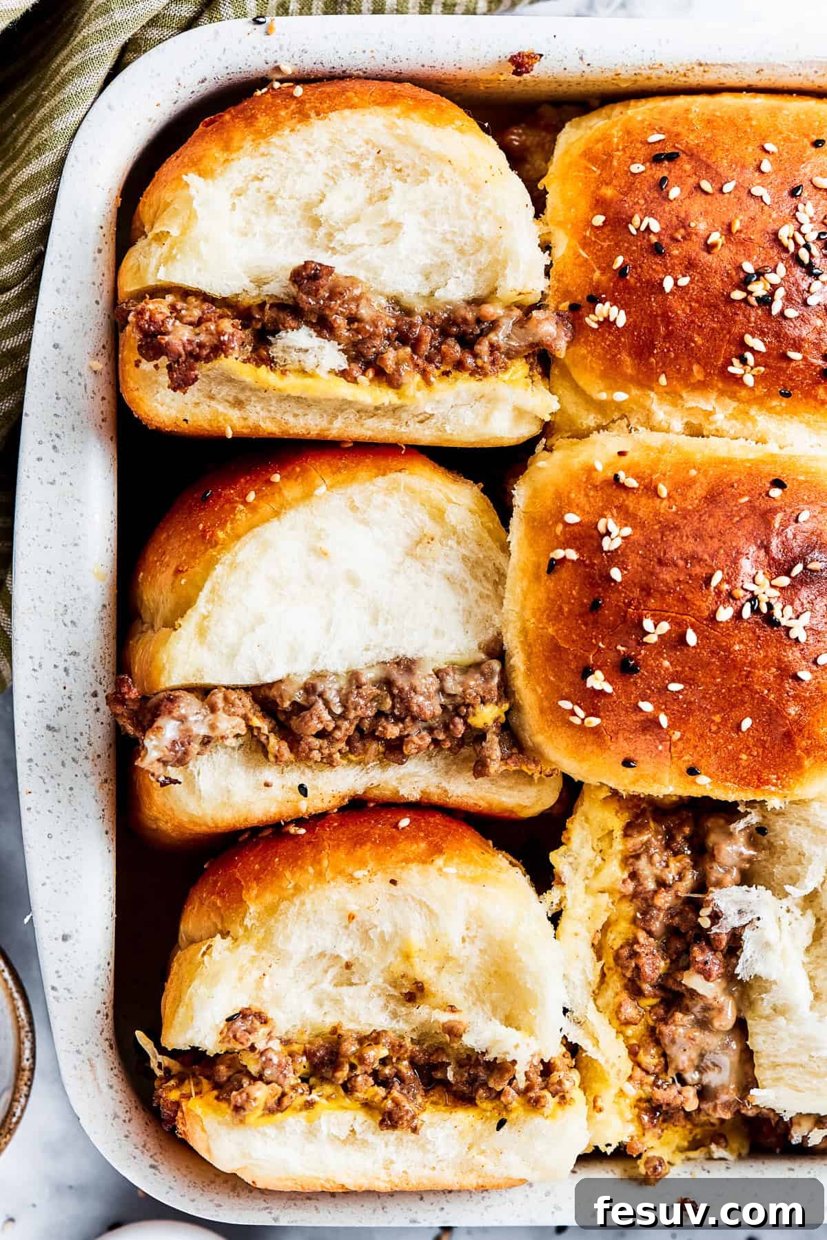 Three perfectly assembled cheeseburger sliders on a wooden board, ready to be served.