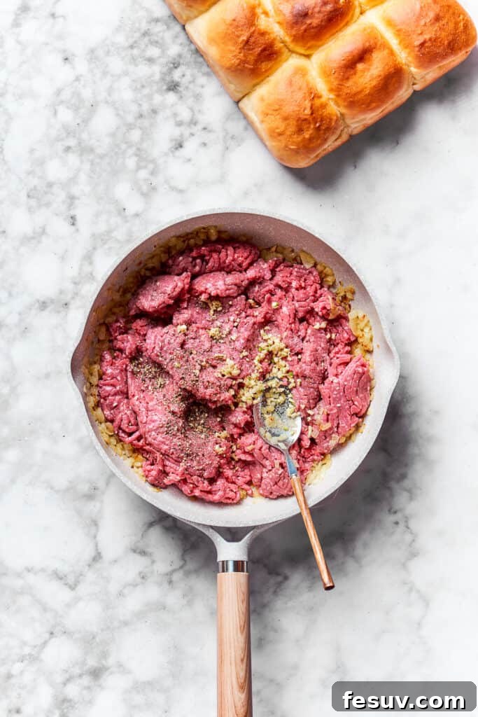 Ground beef being added to the skillet with cooked onions, ready to be browned.