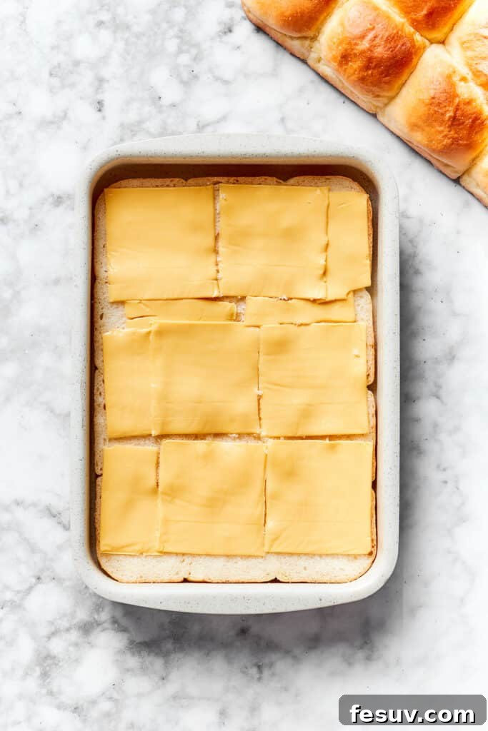 Slices of American cheese carefully placed over the bottom half of dinner rolls in a baking dish.