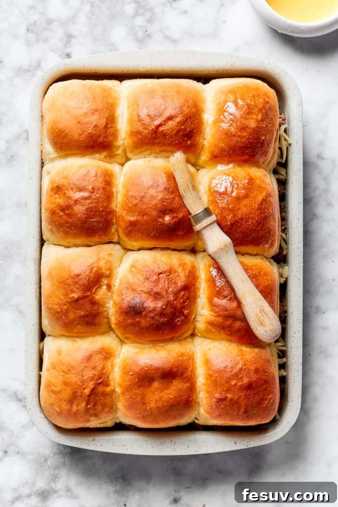 Melted garlic butter being brushed meticulously over the top halves of the dinner rolls.