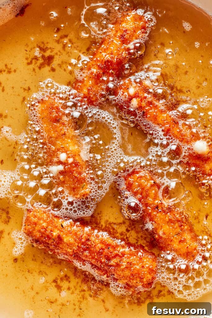 Several breaded mozzarella sticks are frying in hot oil, turning golden brown as they cook.
